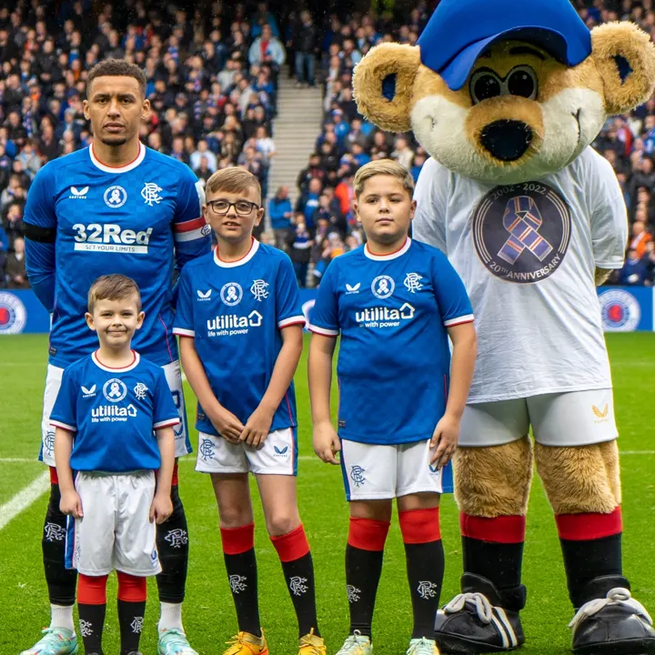A Rangers player with three young mascots and Broxi Bear on the pitch at Ibrox