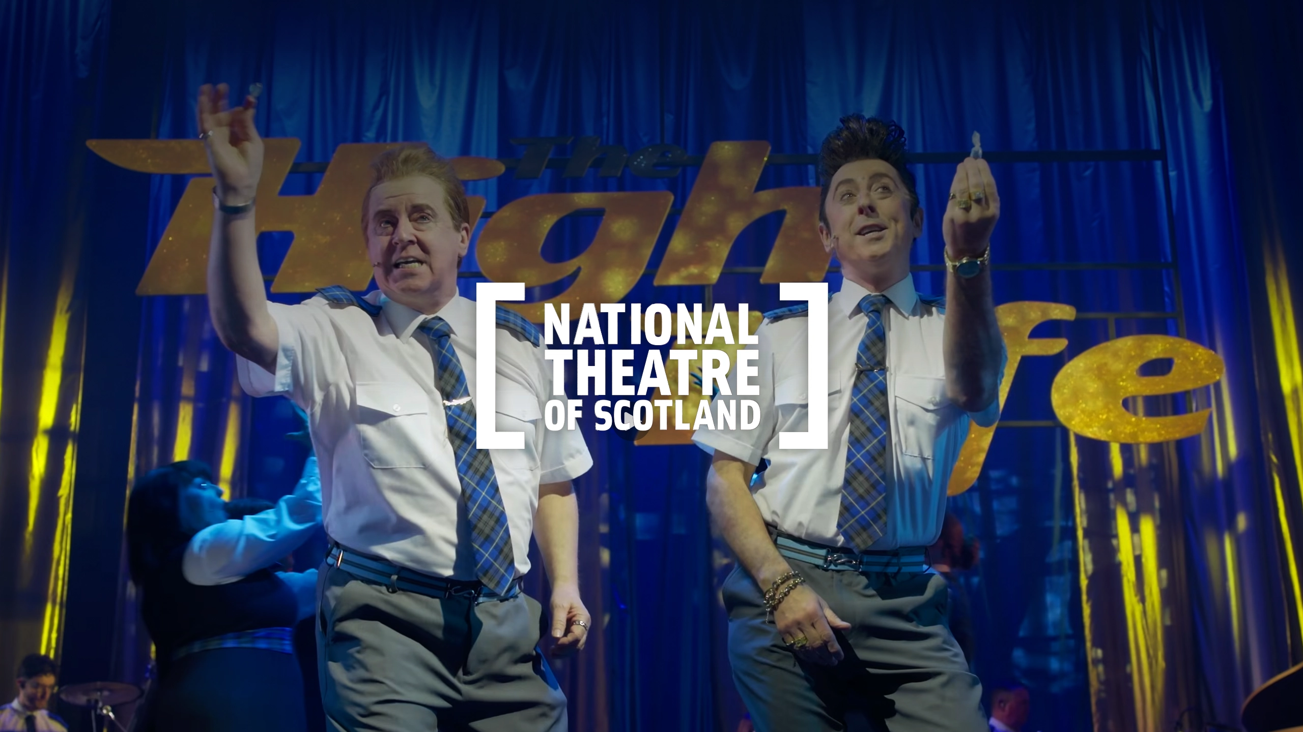 Actors dancing on stage in 'The High Life' with the National Theatre of Scotland logo