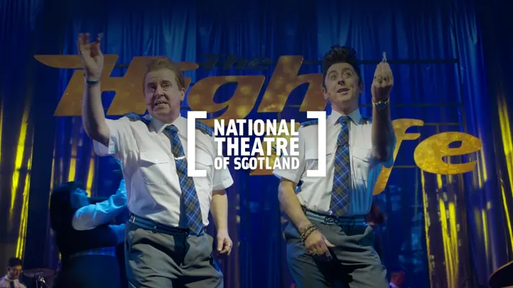 Actors dancing on stage in 'The High Life' with the National Theatre of Scotland logo