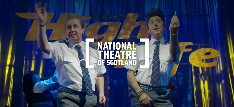 Actors dancing on stage in 'The High Life' with the National Theatre of Scotland logo