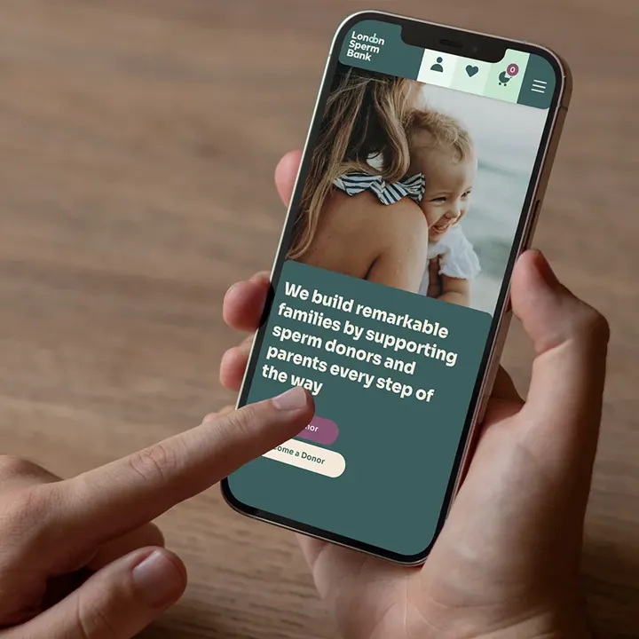 A hand holding a phone showing the London Sperm Bank website home page