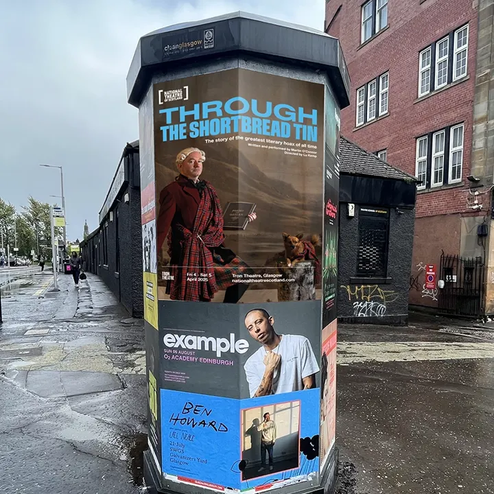 A printed poster in town, wrapped around a pillar, advertising the National Theatre of Scotland's show Through The Shortbread Tin