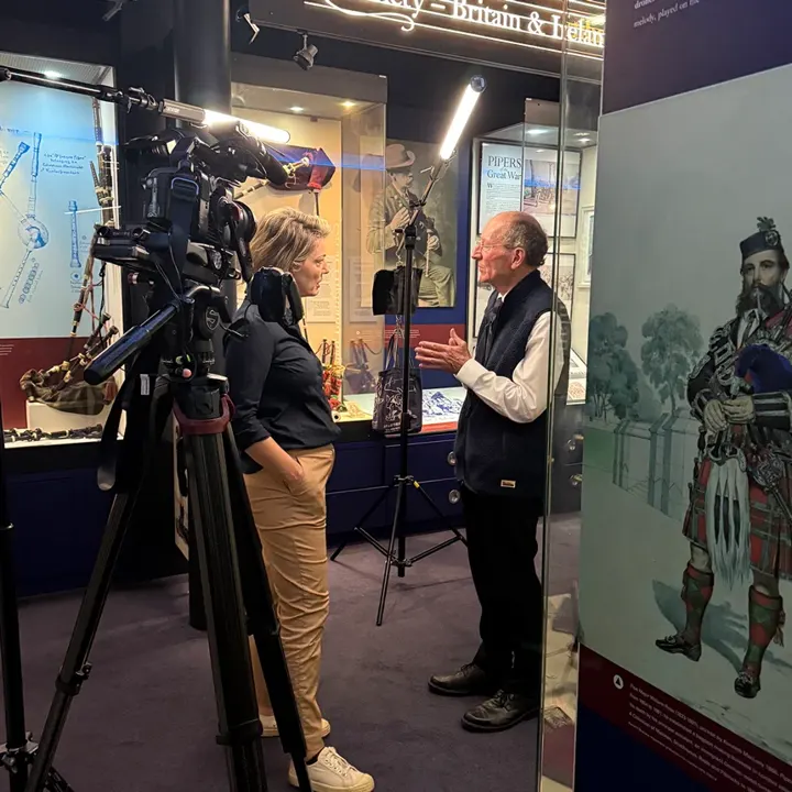 A presenter interviewing a man at the National Piping Centre museum, with a film camera in the foreground