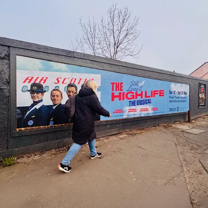 A woman walking past a billboard for 'The High Life: The Musical'
