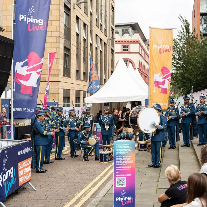 A pipe band in blue uniforms playing outside the Piping Live! festival marquee in Glasgow