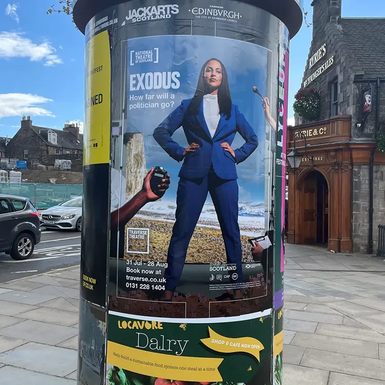 An outdoor poster on a pillar displaying a large printed ad for the National Theatre of Scotland's production of Exodus.
