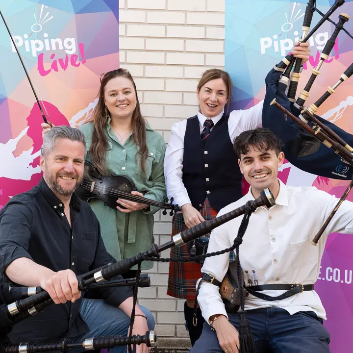Four musicians with bagpipes and a fiddle in front of Piping Live! banners