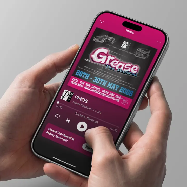 A phone showing a Paisley Musical and Operatic Society 'Grease the Musical' audio advert