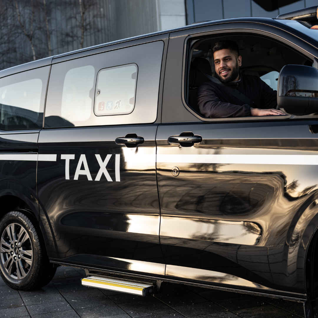 A smiling driver in a black MAXICab taxi