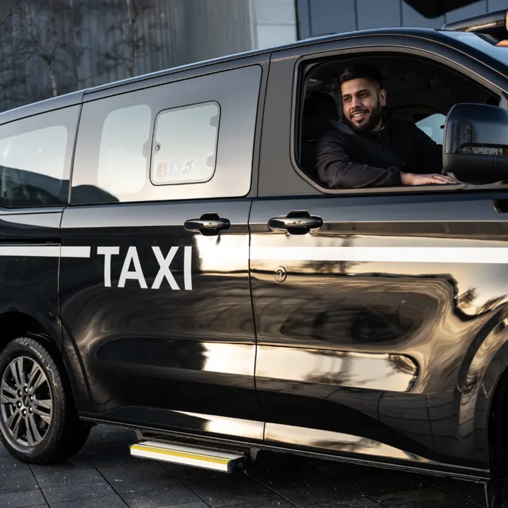 A smiling driver in a black MAXICab taxi