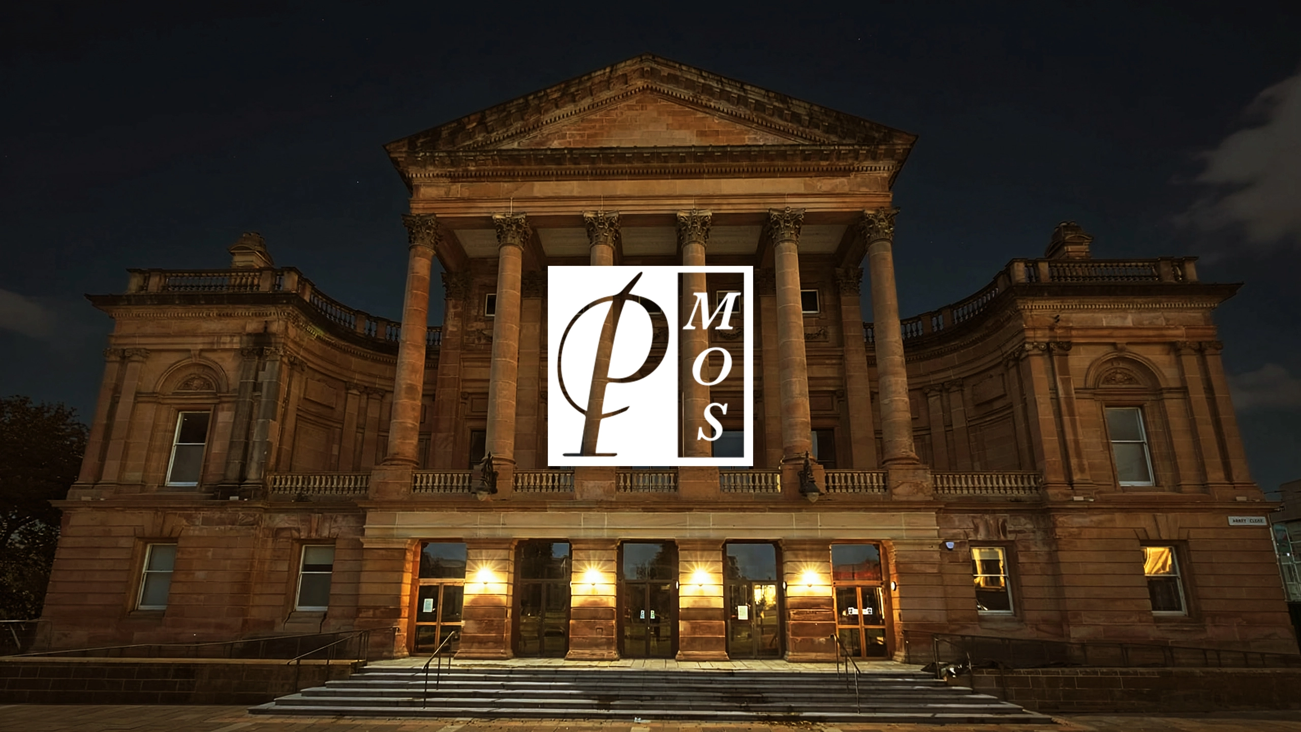Paisley Town Hall lit up at night with the Paisley Musical and Operatic Society logo