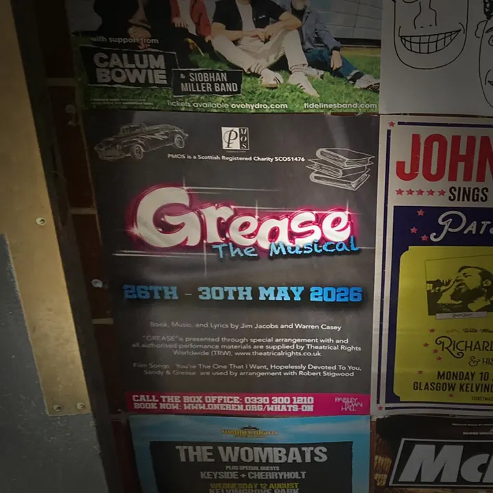 A 'Grease the Musical' poster among gig posters on a wall