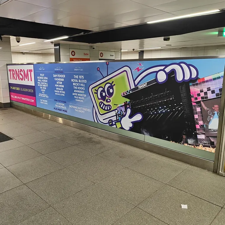 A large TRNSMT 2023 festival advertisement on a subway wall. It lists the July lineup for the Glasgow Green festival, featuring Sam Fender and The 1975, and others.