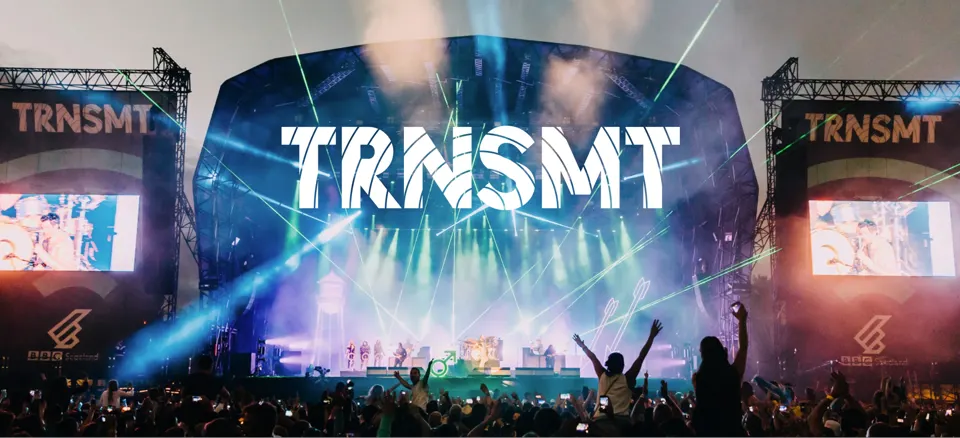 A photograph of one of the night shows at the TRNSMT Festival in Glasgow, showing large TRNSMT branding and people sitting on shoulders to get a better view of the performers