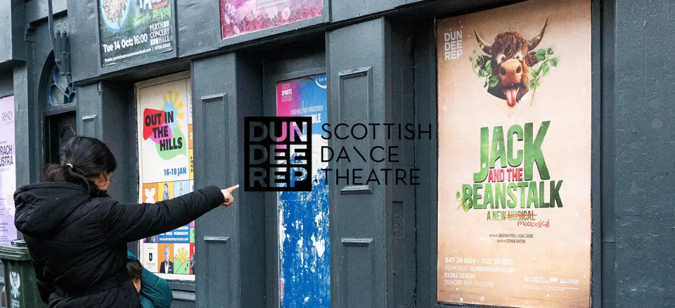 A woman pointing at a Dundee Rep 'Jack and the Beanstalk' poster outside the theatre