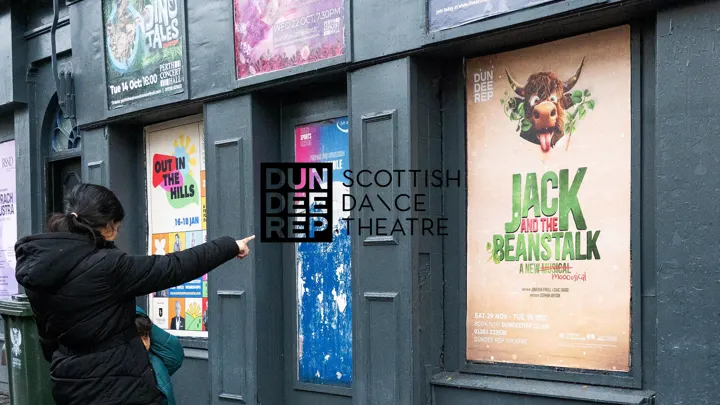 A woman pointing at a Dundee Rep 'Jack and the Beanstalk' poster outside the theatre