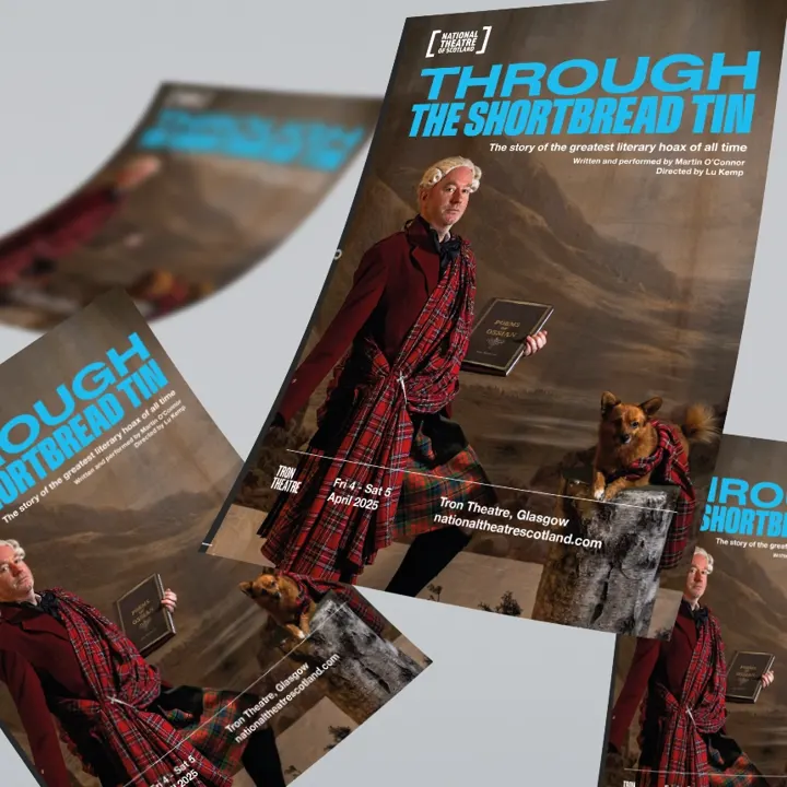 Many printed flyers for a National Theatre of Scotland production titled Through the Shortbread Tin are displayed across a grey surface.