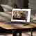 A silver laptop sitting on a wooden coffee table in a living room, playing a YouTube video of people dining together.