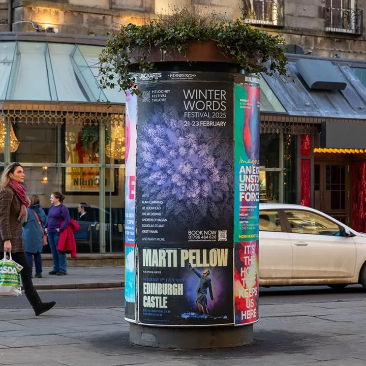 A 'Winter Words Festival 2025' poster on a street column outside a theatre