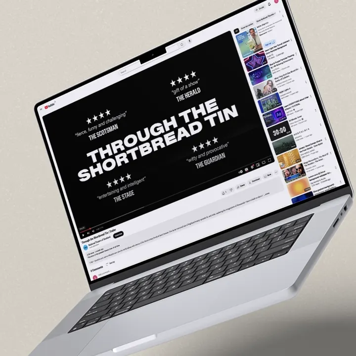 A laptop is displaying a YouTube video trailer for the National Theatre of Scotland's production, Through the Shortbread Tin.
