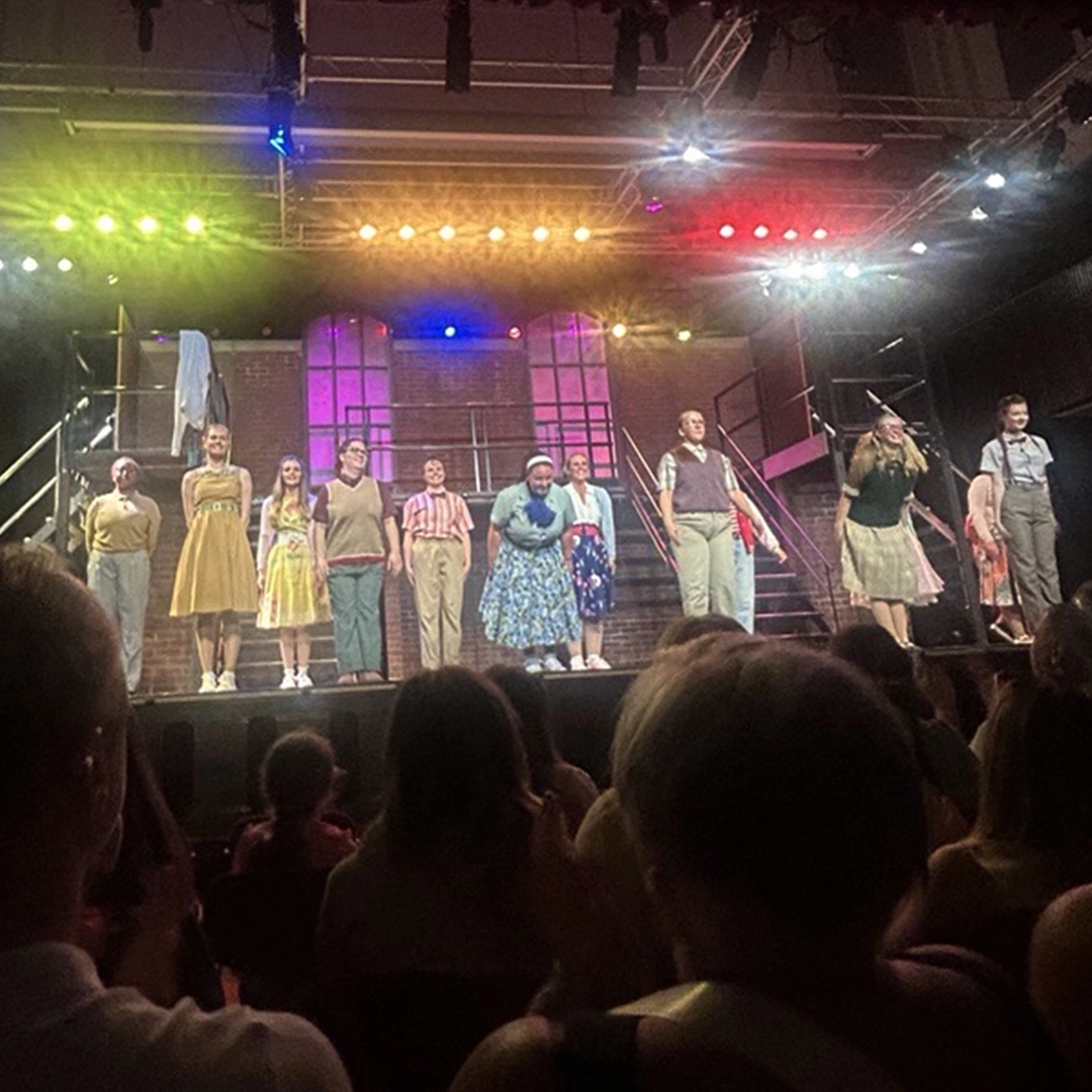 The cast of 'Grease the Musical' on stage taking a bow under coloured lights