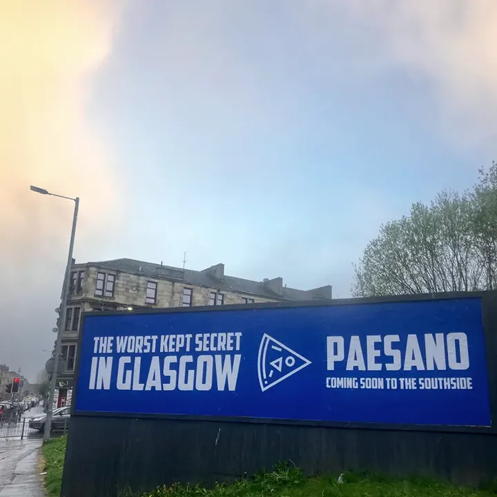 A large blue billboard outdoors advertising The Worst Kept Secret in Glasgow - Paesano Pizza