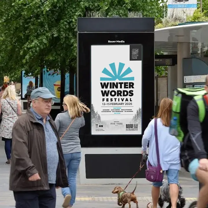 People walking past a digital street screen advertising 'Winter Words Festival', 12 to 15 February 2026