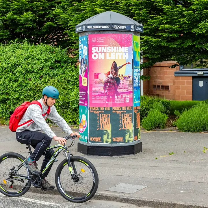 A cyclist passing a street column with a Pitlochry Festival Theatre 'Sunshine on Leith' poster