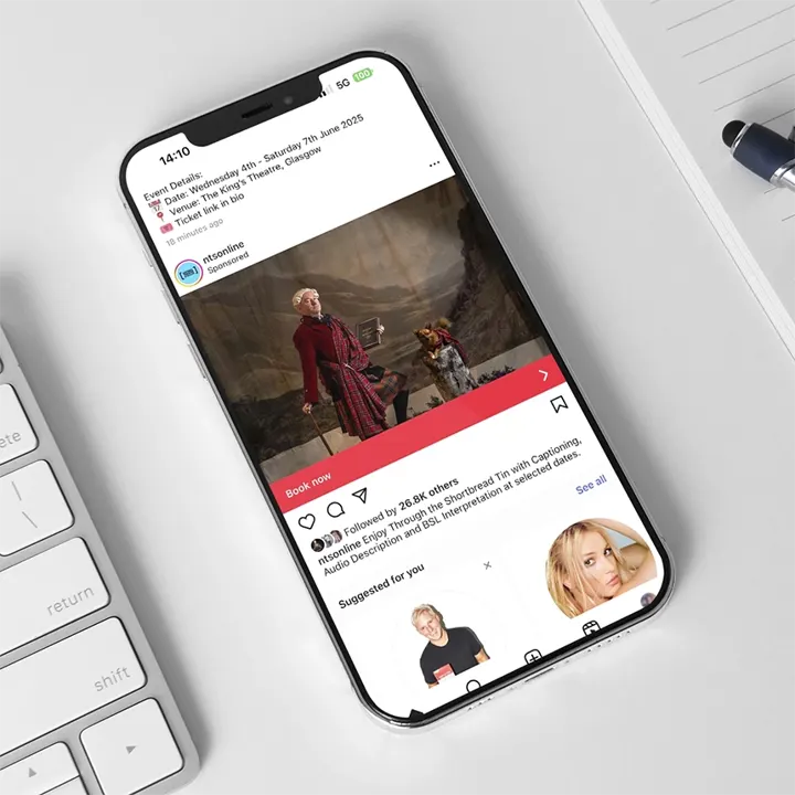 A mobile phone showing a sponsored post for the National Theatre of Scotland's show Through The Shortbread Tin, with a call to action to Book Now
