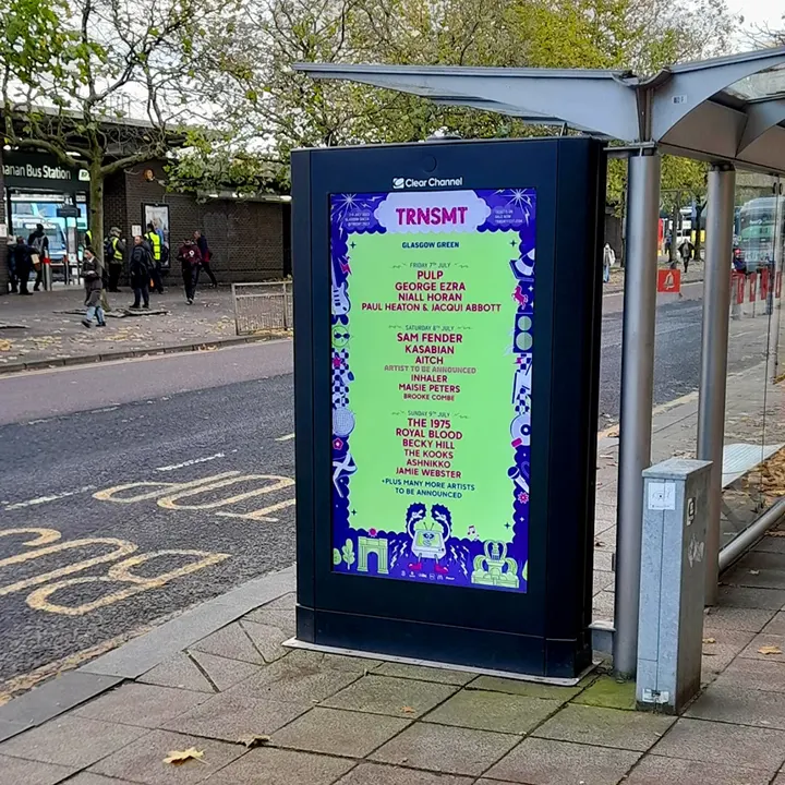 A vertical digital advertisement for TRNSMT 2023 at a city bus stop. The bright green poster lists the full three-day lineup for TRNSMT Festival at Glasgow Green, including George Ezra, Niall Horan, and Royal Blood.