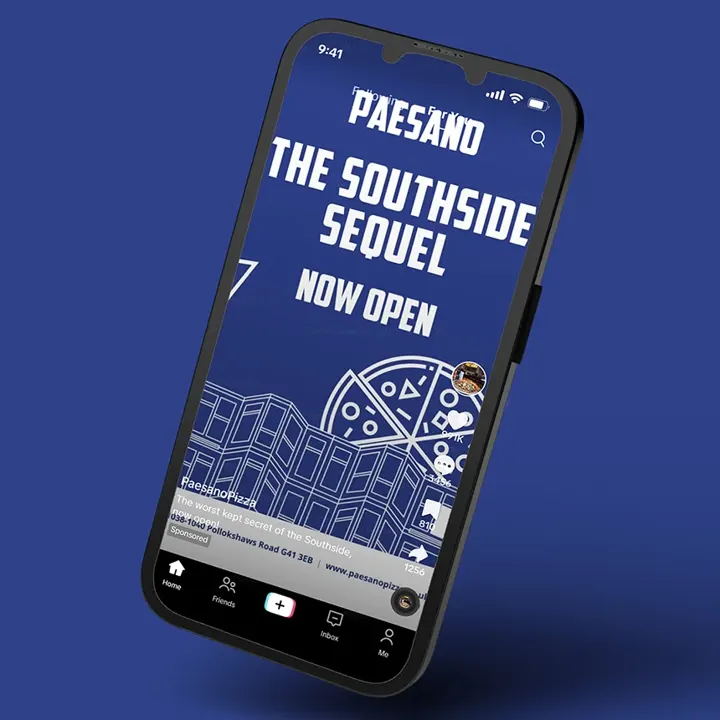 A mobile phone against a blue background displays a social media post for Paesano Pizza. The screen features large white text on a blue background that reads Paesano, The Southside Sequel, Now Open.